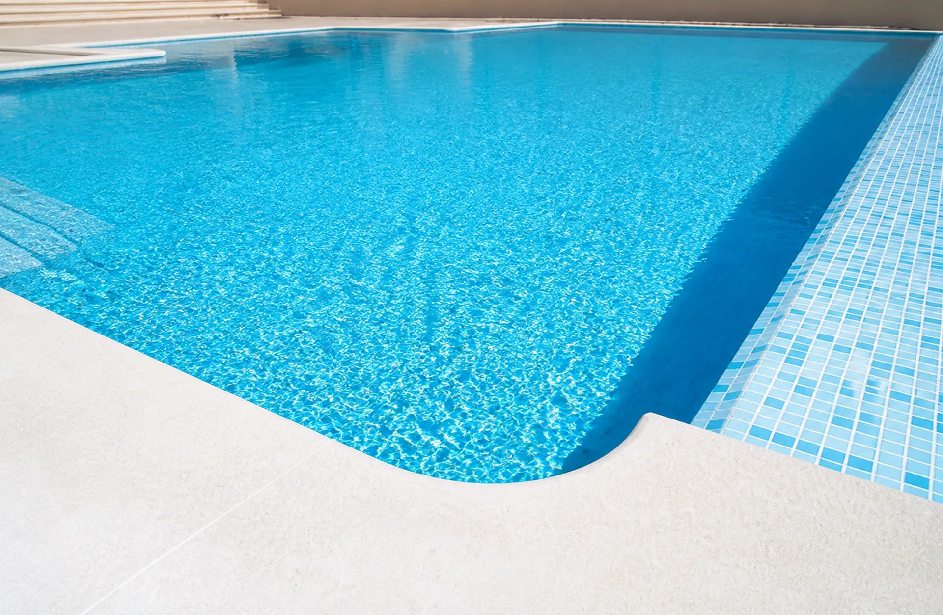 Sunlit swimming pool with mosaic tiling and a stone deck